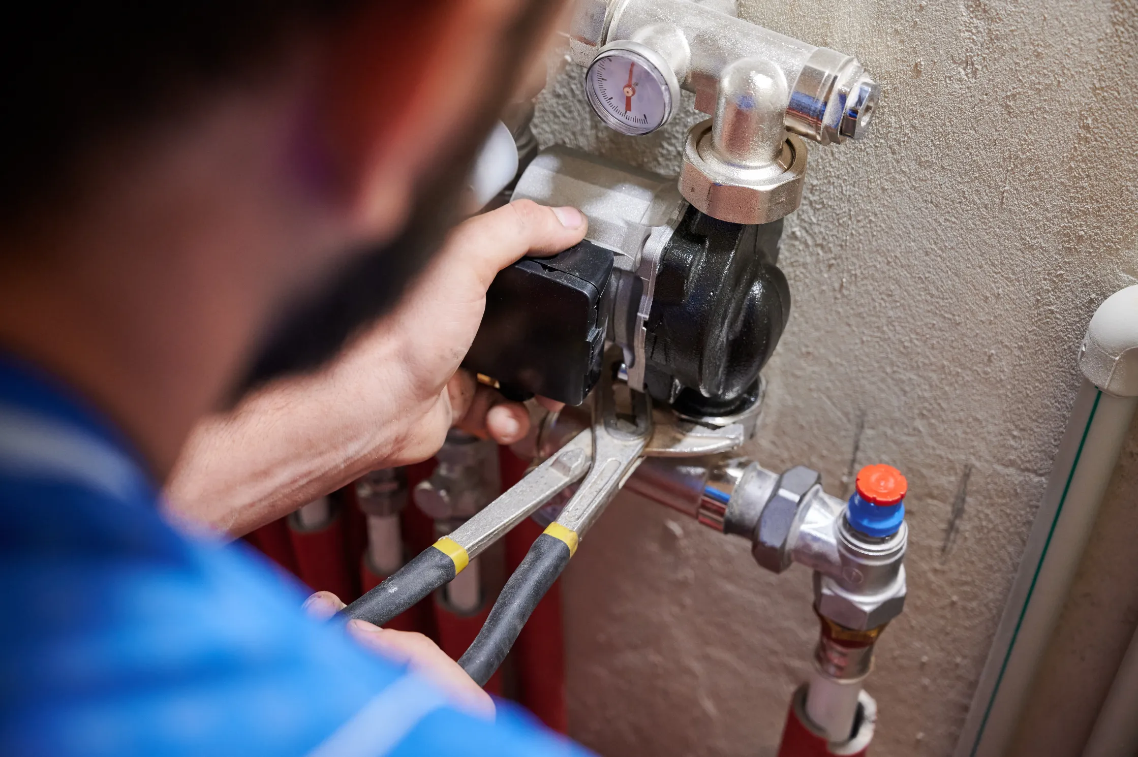 A plumber using a wrench to adjust a valve on a gas boiler system with visible pipes and a pressure gauge. Close-up view focused on the hands and tools, specializing in water damage restoration.