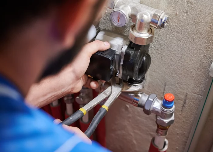 A plumber using a wrench to adjust a valve on a gas boiler system with visible pipes and a pressure gauge. Close-up view focused on the hands and tools, specializing in water damage restoration.